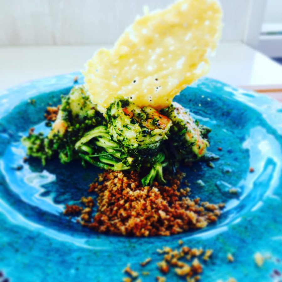 Zucchini noodles with prawns and a parmesan crips on a bright blue plate